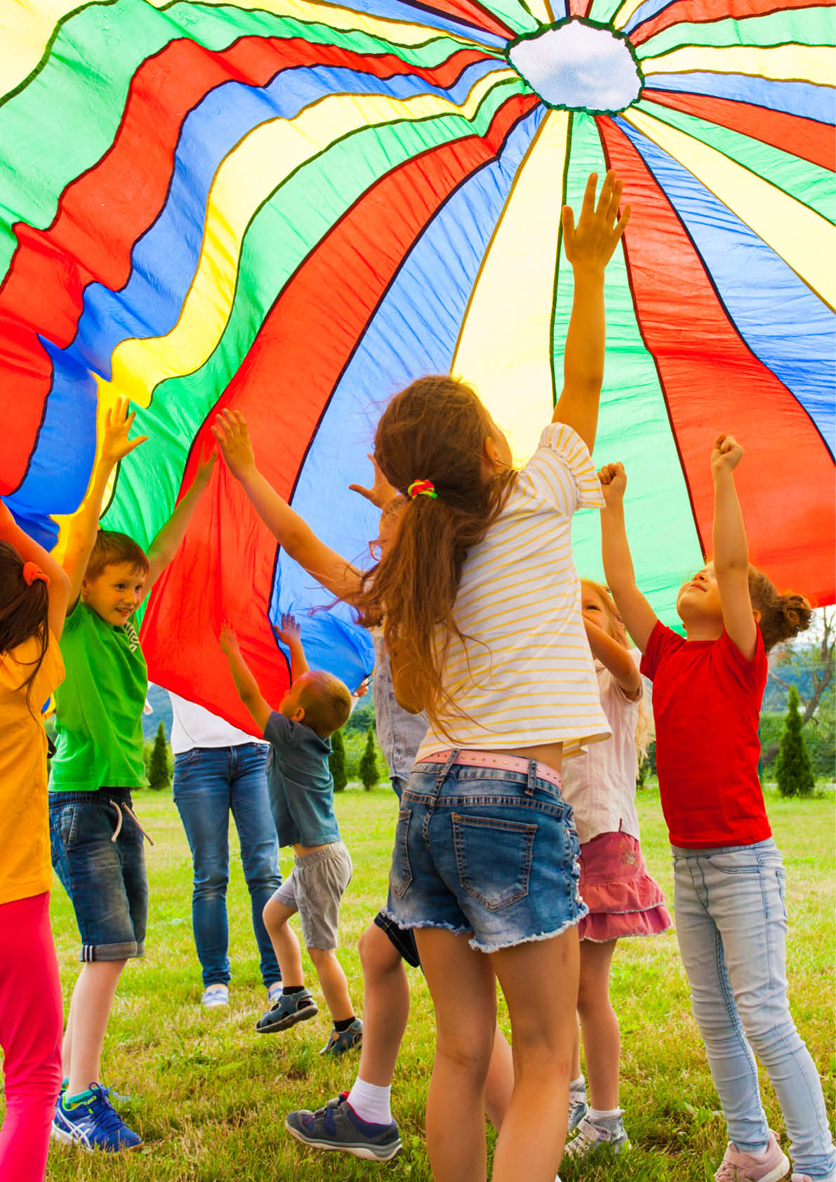 Joyous classmates jumping under colorful parachute