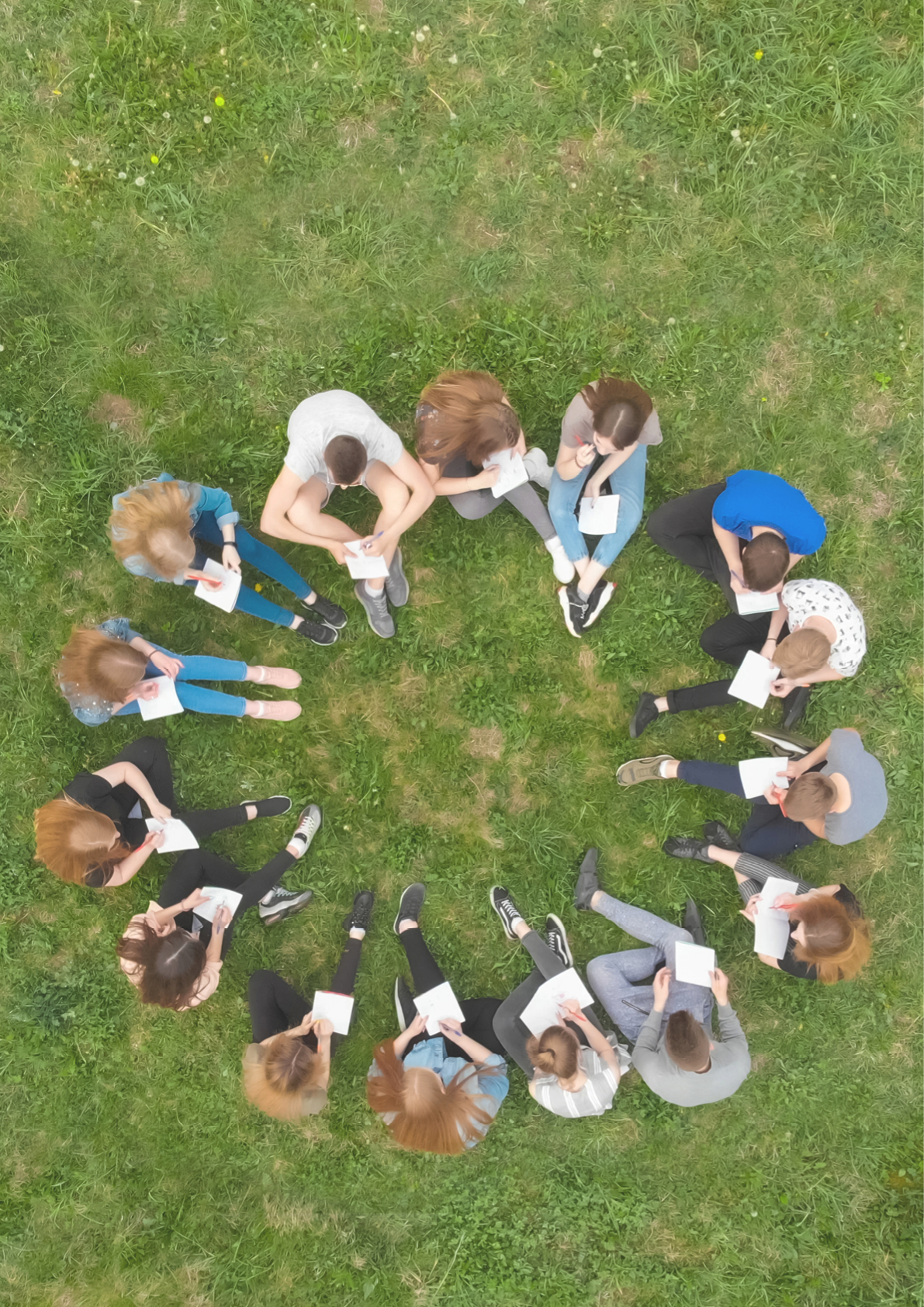 A group of students are sitting in a circle and books on the grass.