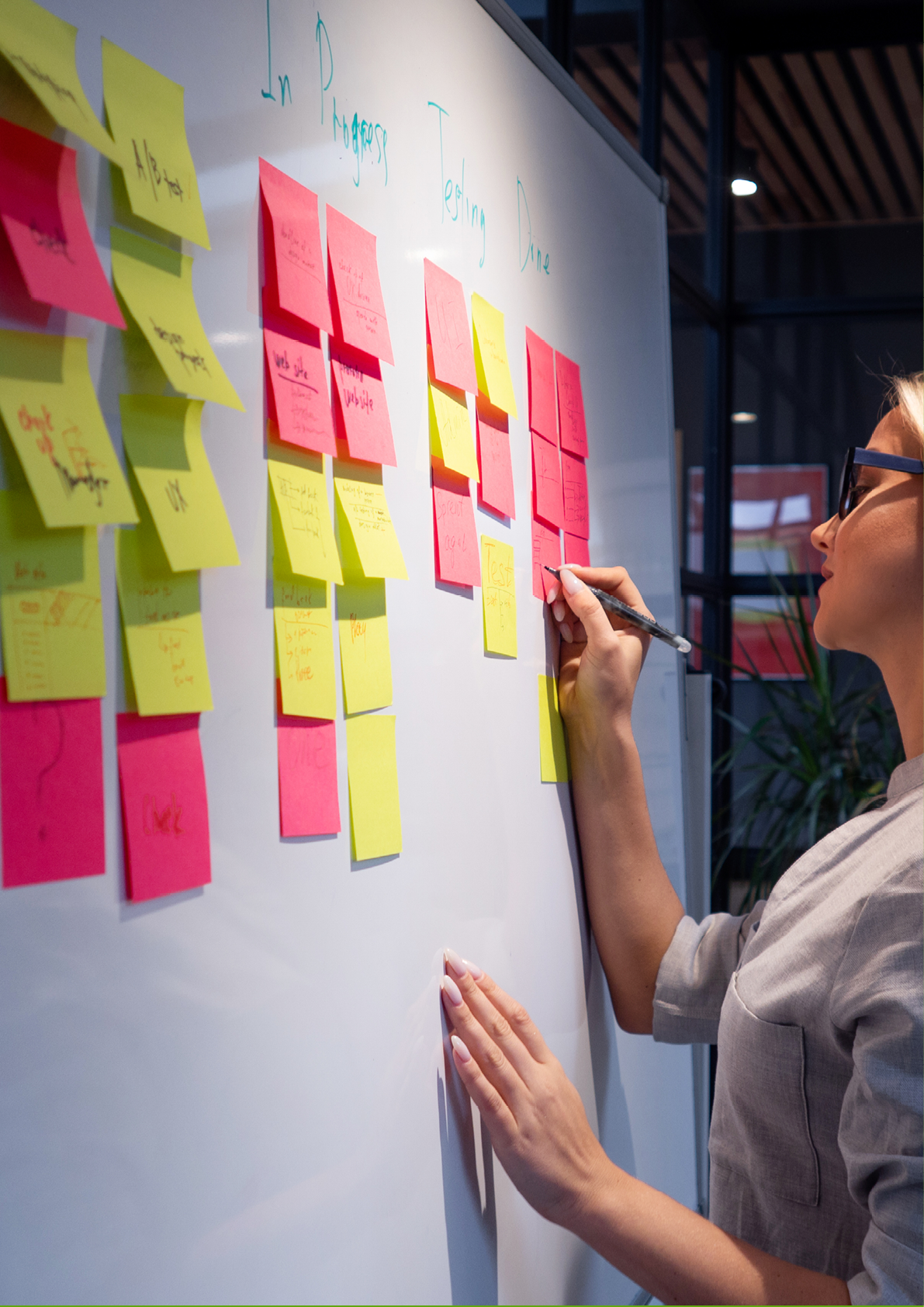 Project management, product development methodologies. A young woman makes notes on a white magnetic marker Board and glue colored sticky leaves.