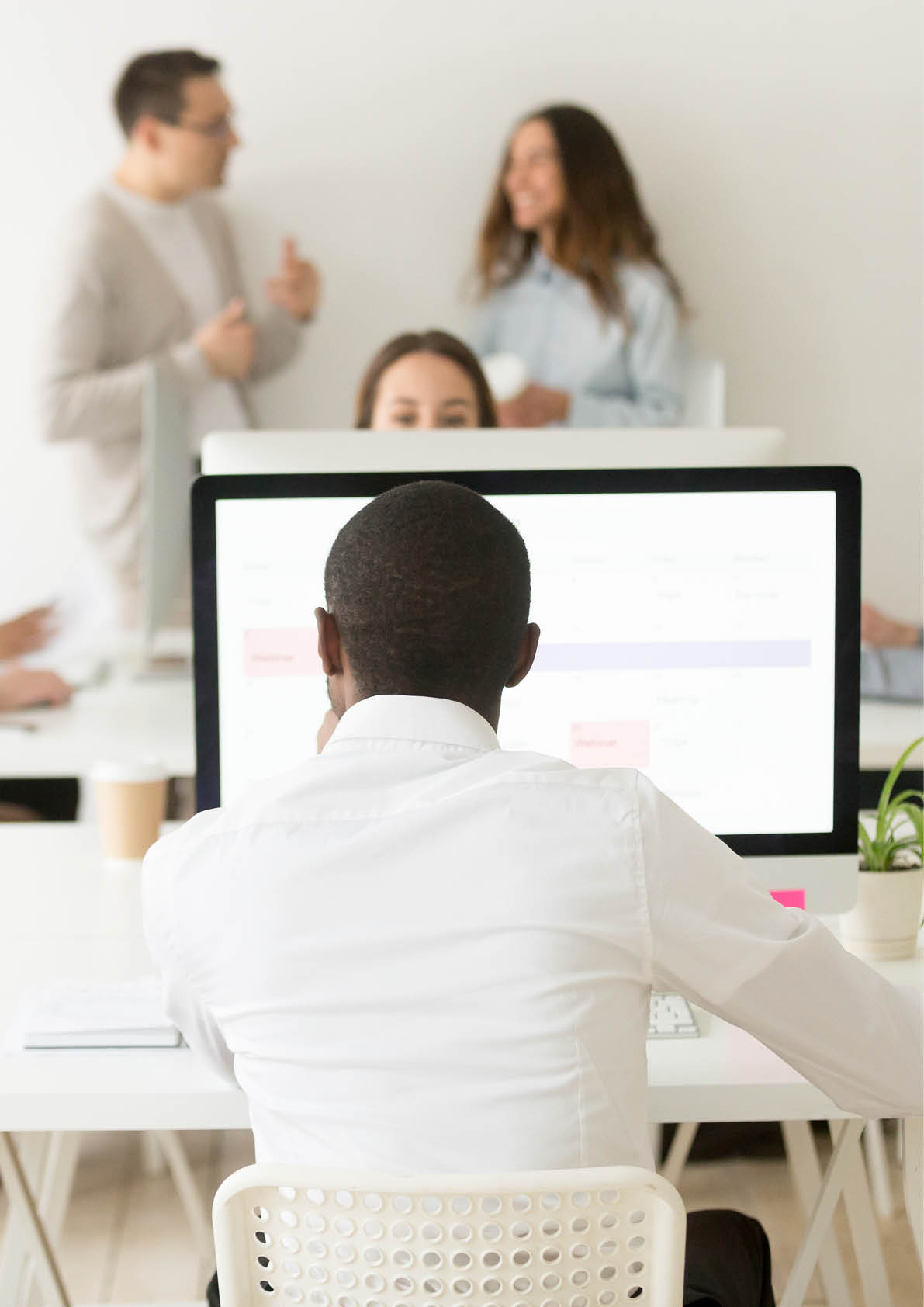 Rear view at african american employee working on computer in multiracial office, black employee focused on business planning using pc application with diverse colleagues around in shared coworking