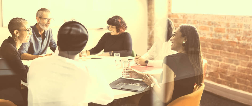 Smiling businesspeople sitting together in a meeting room. Group of successful businesspeople attending their morning briefing in a modern office. Cheerful colleagues working together.