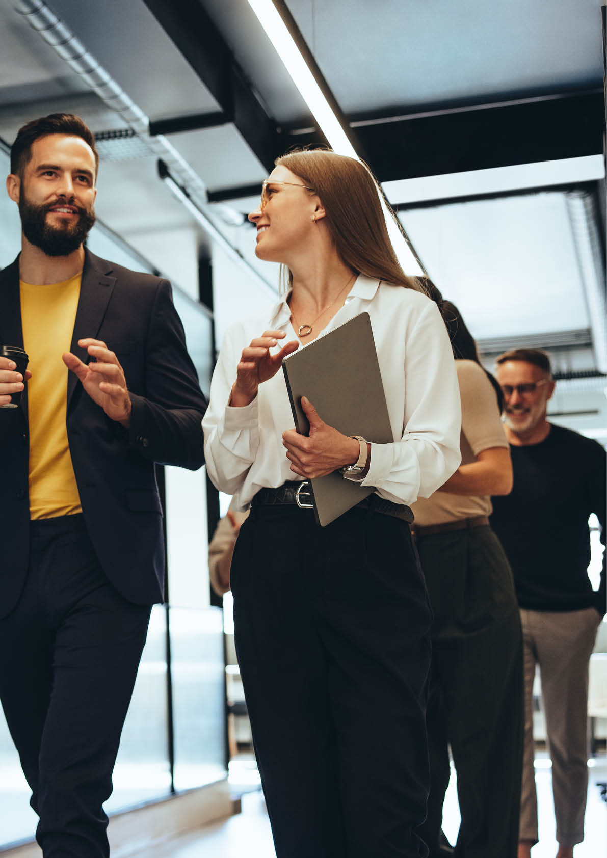 Young professionals having a discussion in a modern office. Two happy young businesspeople smiling while walking together in a hallway. Cheerful colleagues collaborating on a new project.