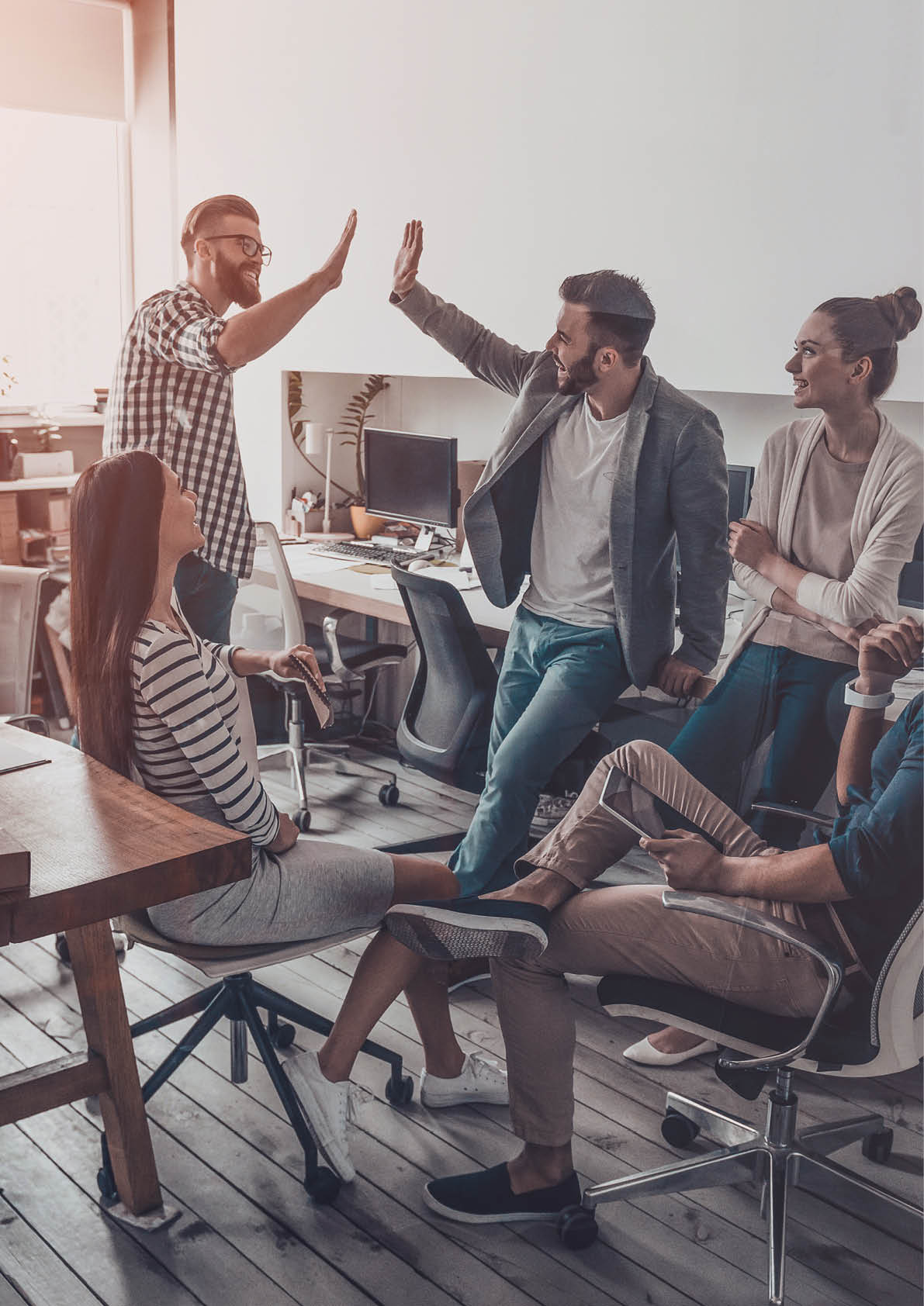 We did it! Two cheerful young business people giving high-five while their colleagues looking at them and smiling 