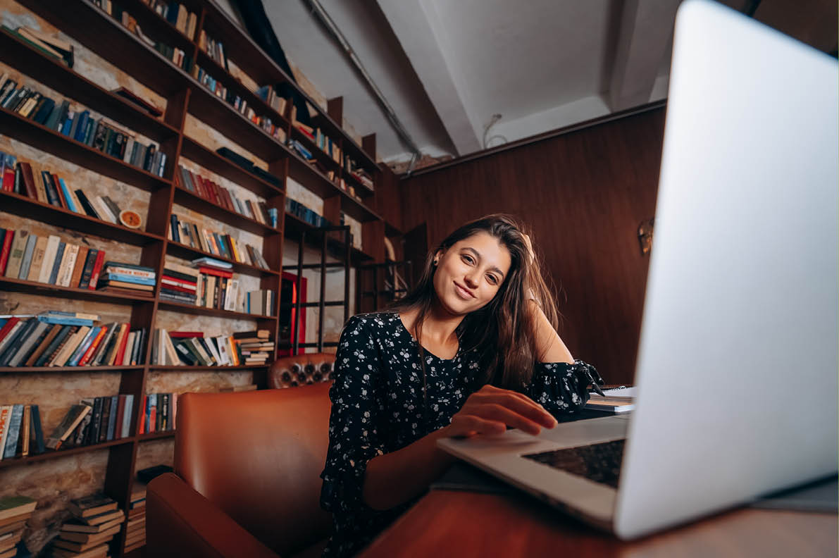 Young beautiful woman in glasses works at the laptop while sitting at the table