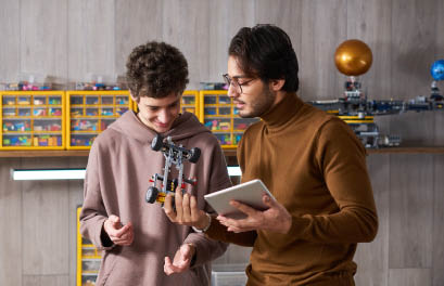 Young teacher using digital tablet and trying to connect artificial car together with teenager for science project