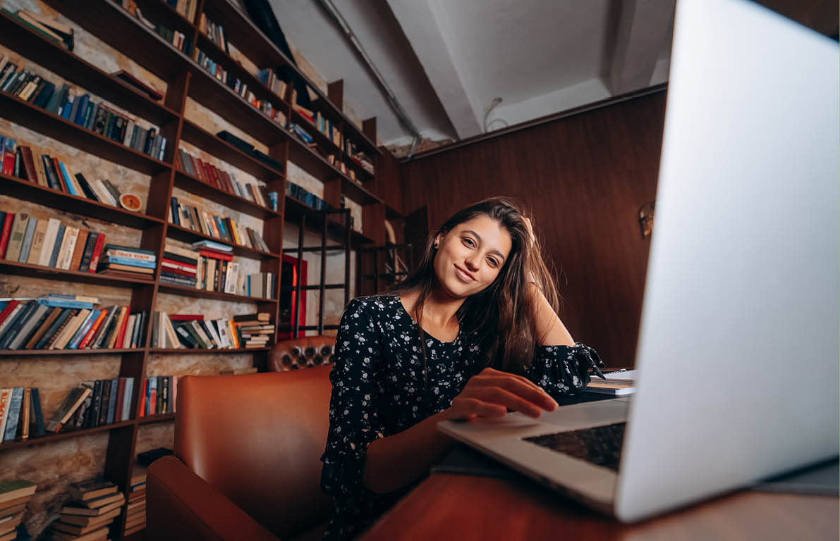 Young beautiful woman in glasses works at the laptop while sitting at the table