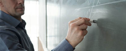 Contemporary teacher with piece of chalk writing formula on blackboard