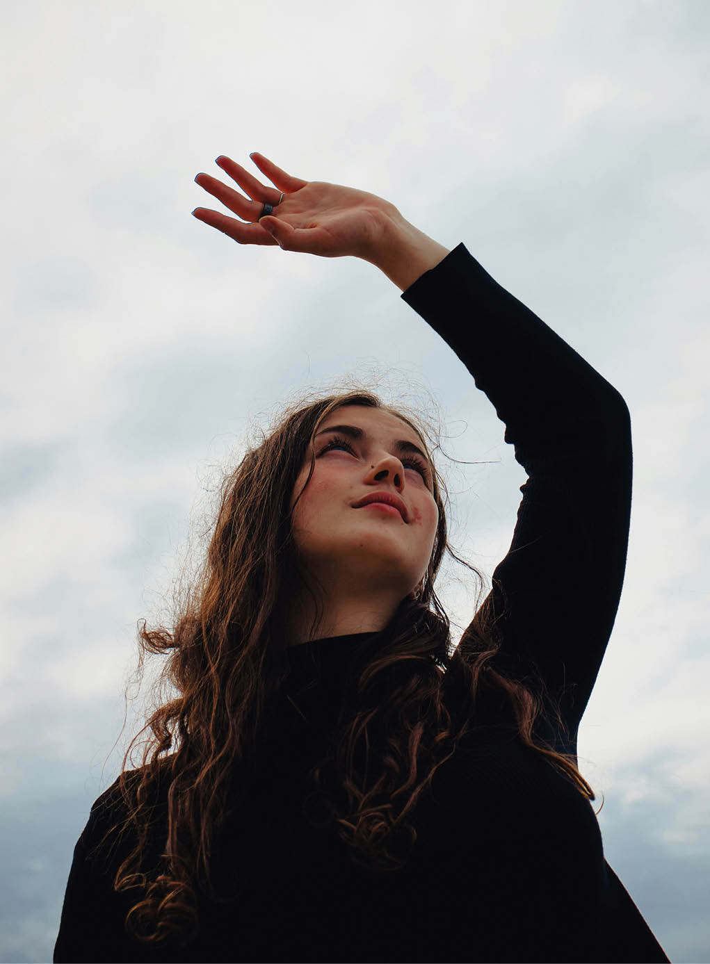 A woman with long hair and a black shirt stands in front of a cloudy sky. AI generated content