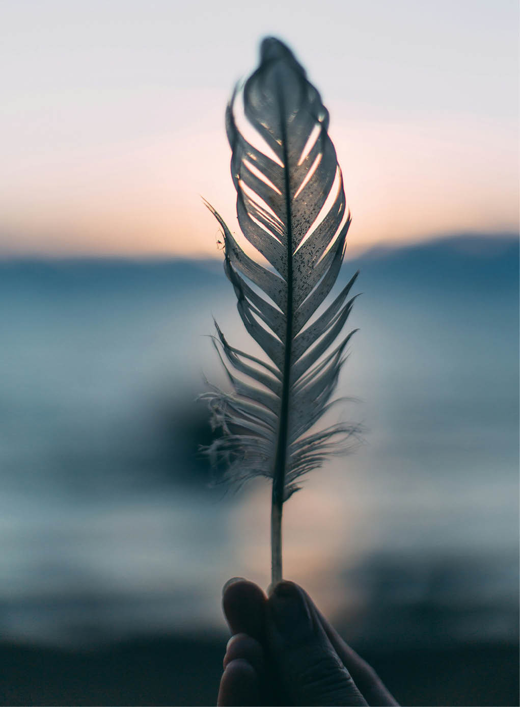 A hand holding a feather in front of a body of water. AI generated content