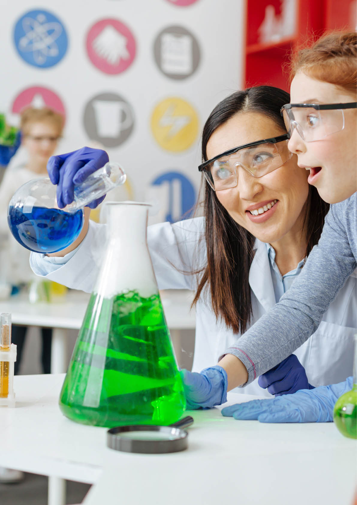 Wonders of chemistry. Charming chemistry teacher pouring blue chemical into a green one and smiling while her student being excited about the reaction