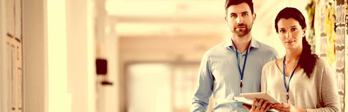 Two teachers standing in a school corridor, they are both dressed smart casual and look serious