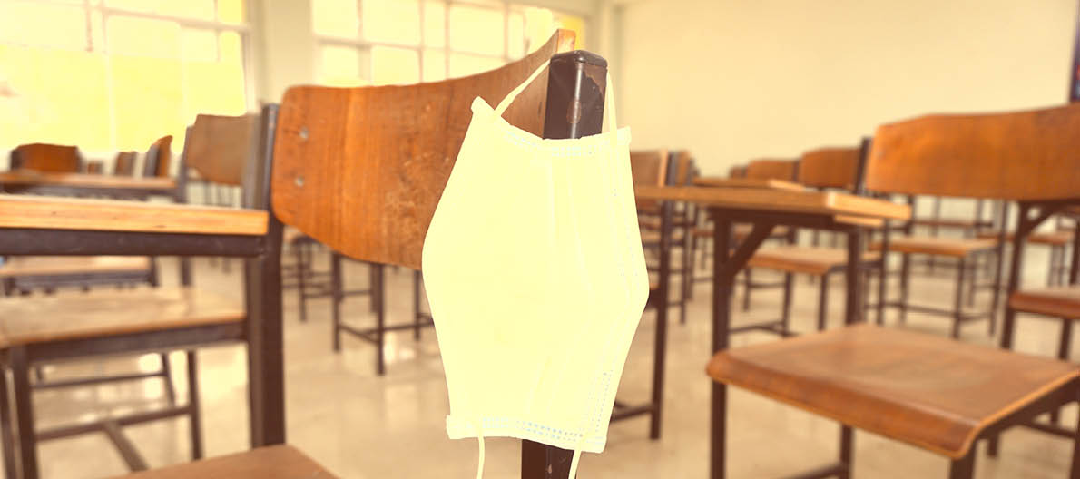 The used medical face mask hangs on the wood lecture chairs in the empty classroom. Concept during the Coronavirus Disease COVID-19 outbreak and pandemic in the 2020s. Back to school concept.