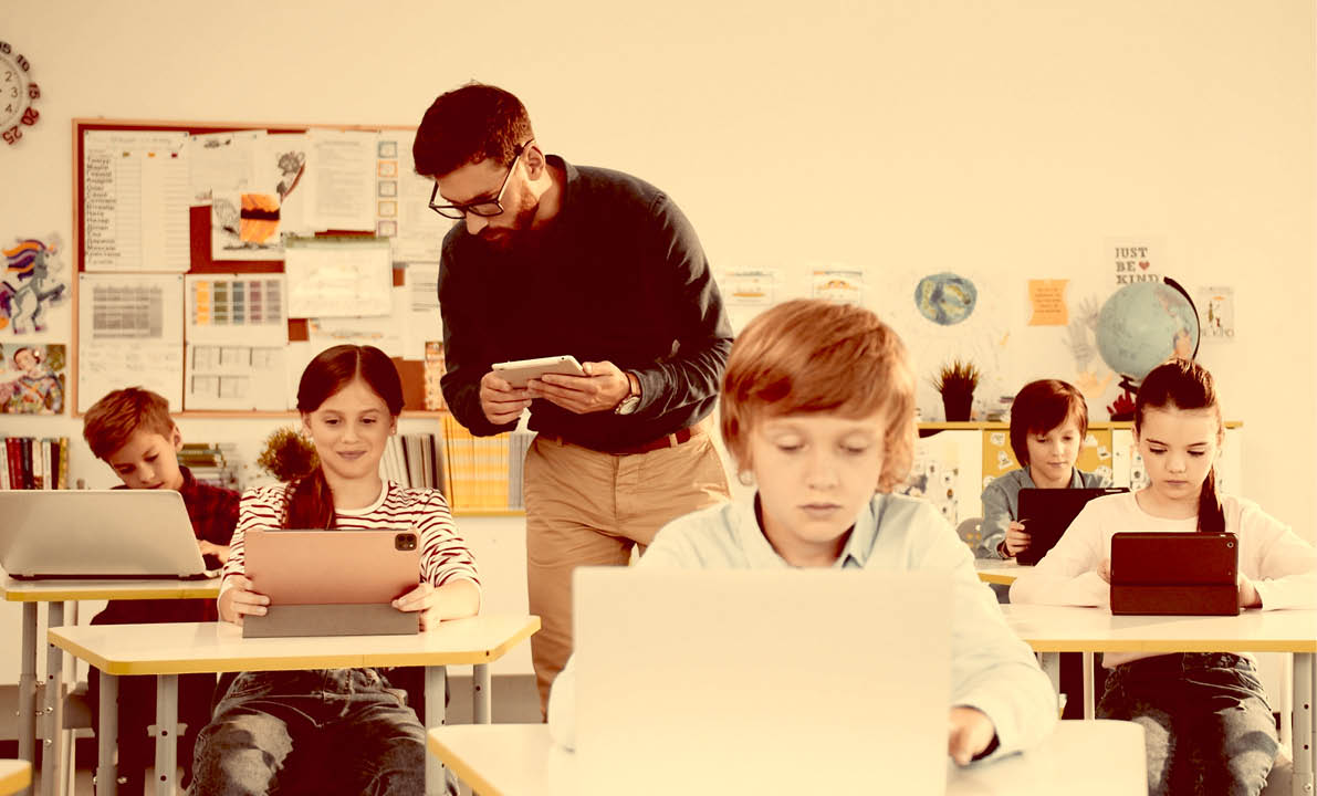 Elementary school computer science class. junior students girls and boys use laptop at lesson. Male teacher explaining and helping schoolgirl at class using tablet Internet technology Modern education