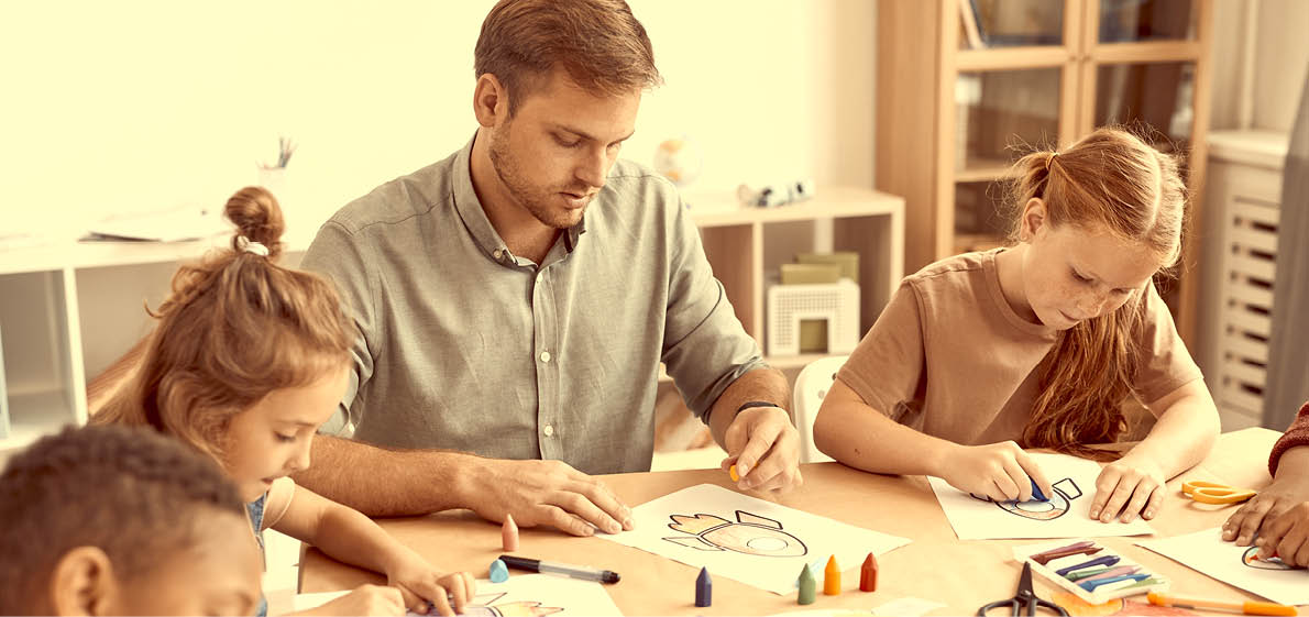 Portrait of male teacher working with multi-ethnic group of children drawing pictures during art class in school or development center, copy space