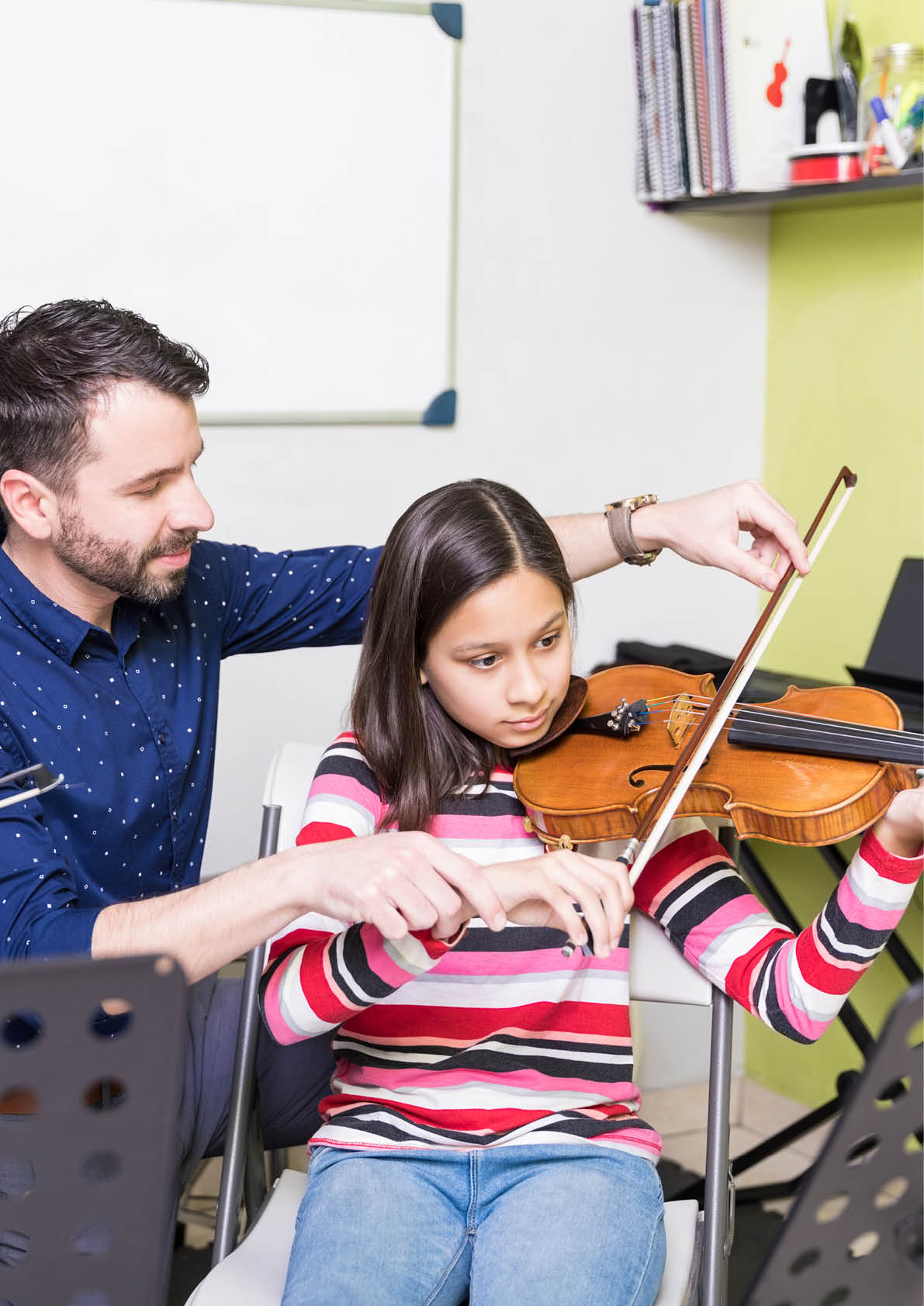 Hispanic girl taking training of playing violin from male teacher in school