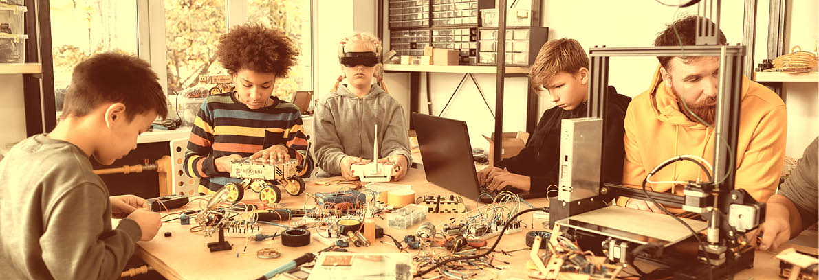 Young technicians building robots and vehicles, using soldering iron to join chips and wires, testing toys together with a male teacher at a stem robotics class. Inventions and creativity for kids