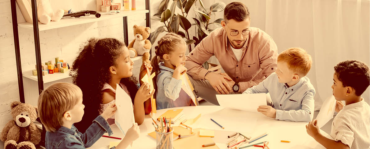 teacher and interracial preschoolers at table with paints and papers in classroom
