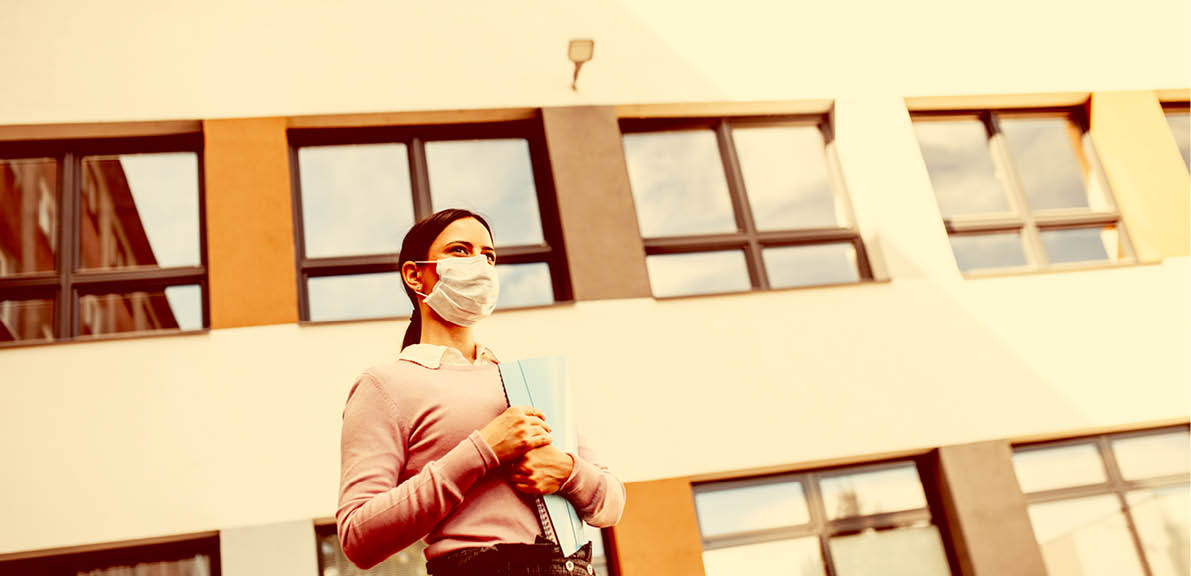 Low angle view of teacher with face mask after lockdown, walking in front of school.