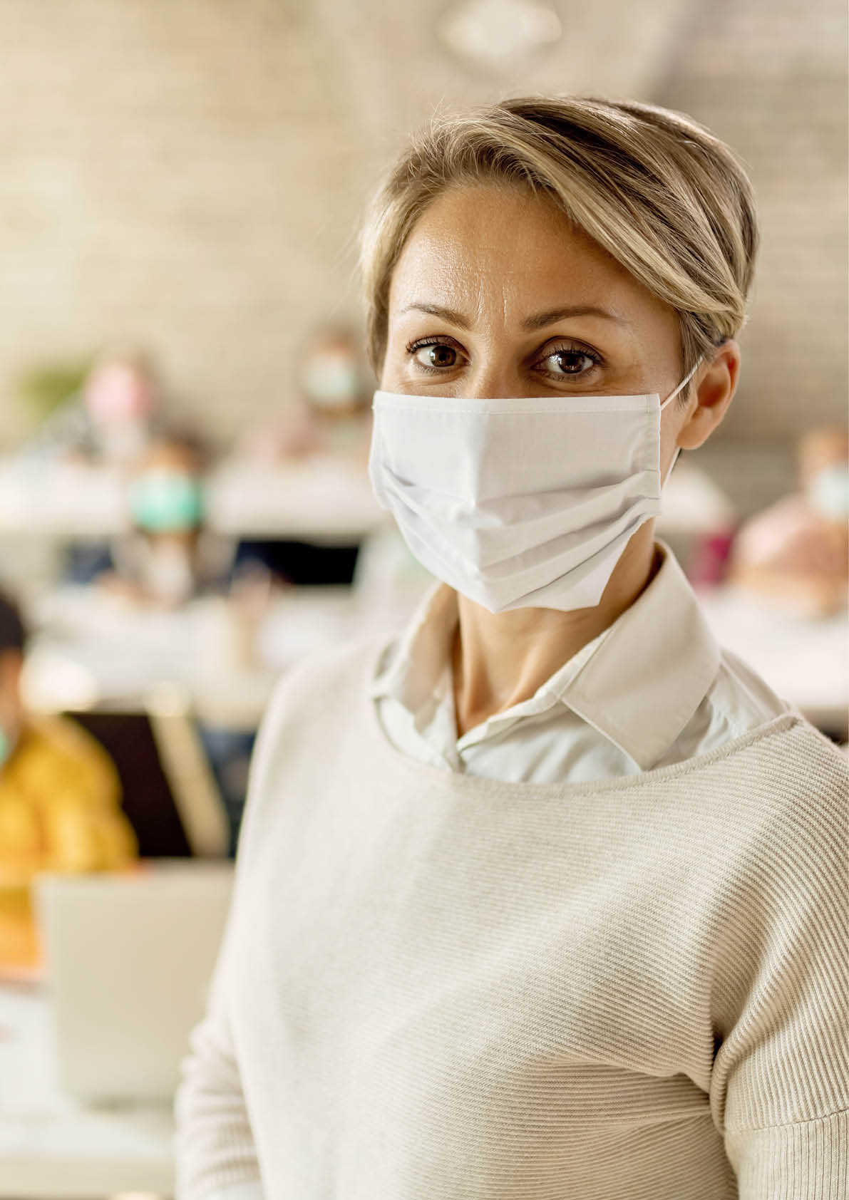 Female teacher wearing a face mask while teaching children at elementary school and looking at camera. 