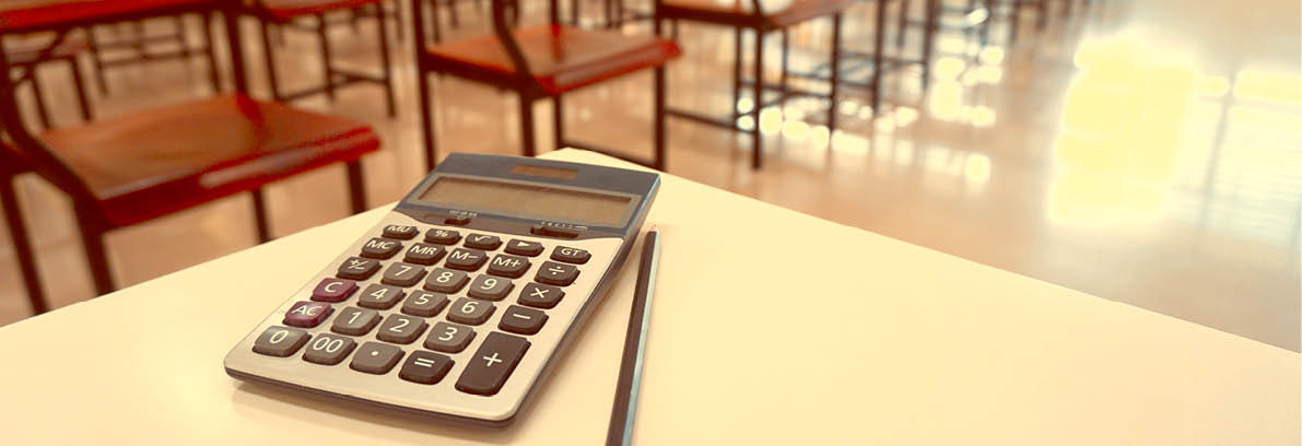 The calculator and pencil on the teacher's desk with the wood lecture chairs place distance in the empty classroom. Back to school, business, and finance accounting concept. Copy space in Thailand.