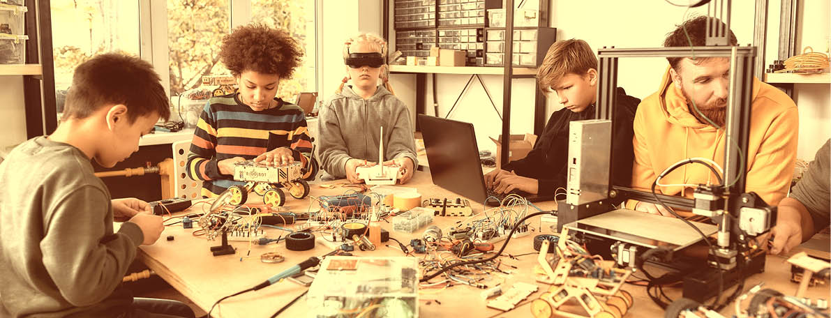 Young technicians building robots and vehicles, using soldering iron to join chips and wires, testing toys together with a male teacher at a stem robotics class. Inventions and creativity for kids