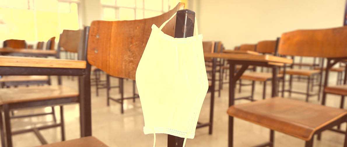 The used medical face mask hangs on the wood lecture chairs in the empty classroom. Concept during the Coronavirus Disease COVID-19 outbreak and pandemic in the 2020s. Back to school concept.